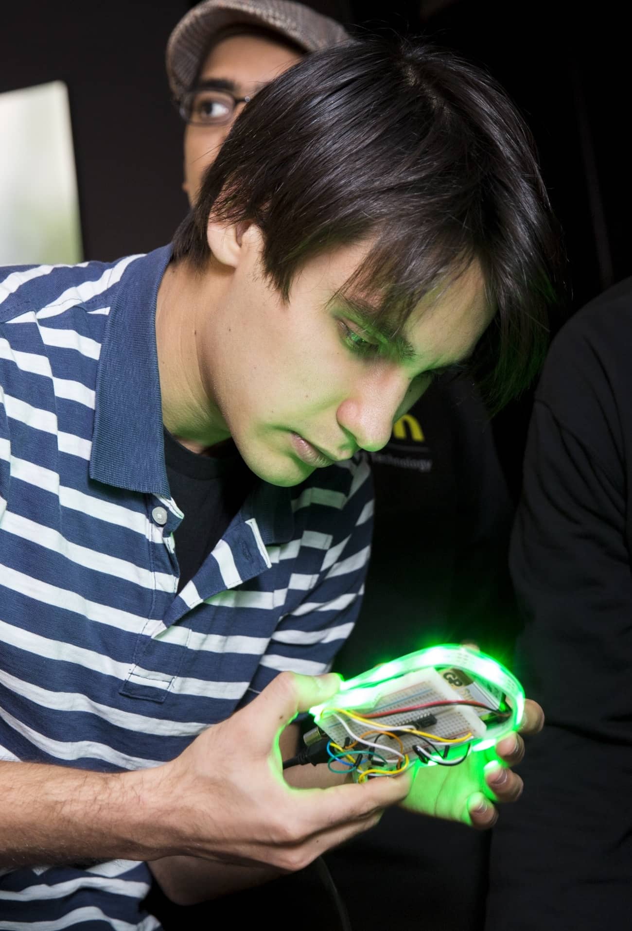 Picture of a student holding and examining a circuit board with a green wrap-around light